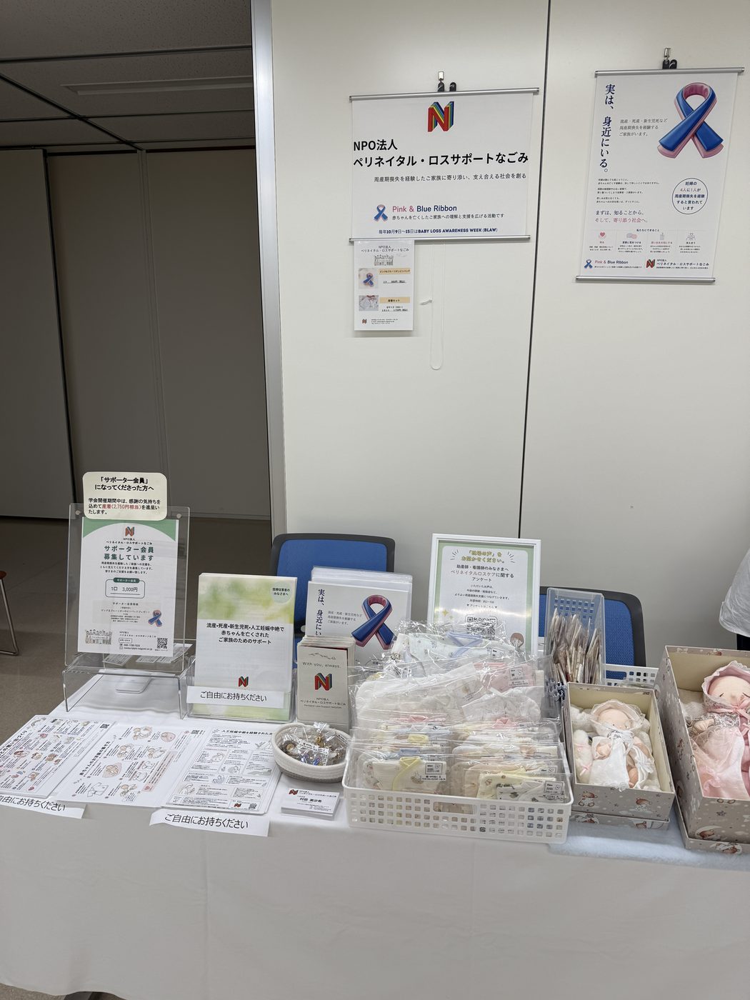 日本助産学会に出展したNPO法人ペリネイタル・ロスサポートなごみのブース全景。サポーター会員の案内やパンフレット、産着などが並び、ピンク＆ブルーリボンの啓発ポスターが掲示されている。
